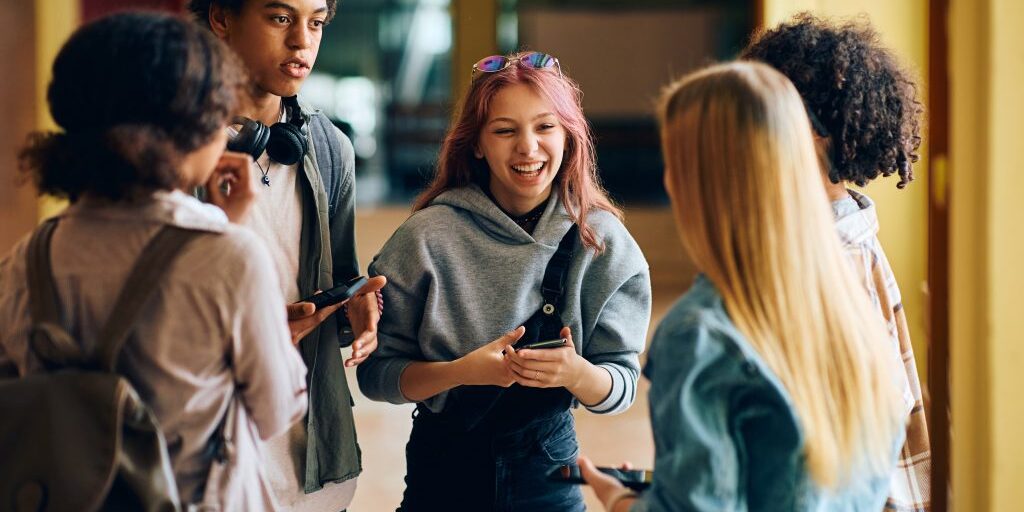 Cheerful high school students have fun while talking in hallway.