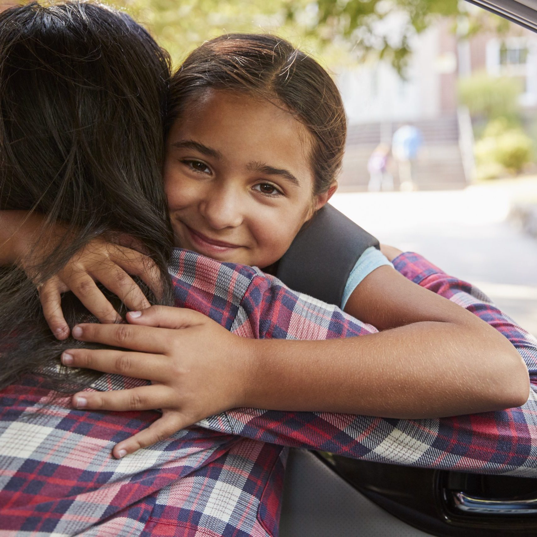 A mother hugs their daughter through a car window.